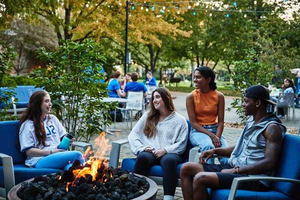 Four students sit around a lit firepit ourside of a 博彩网址大全 residence hall